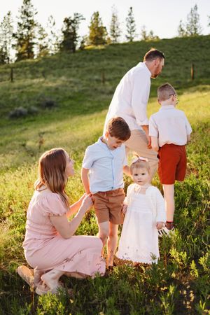 Family enjoying a sunset moment together on a grassy hillside with pine trees in the background during golden hour.