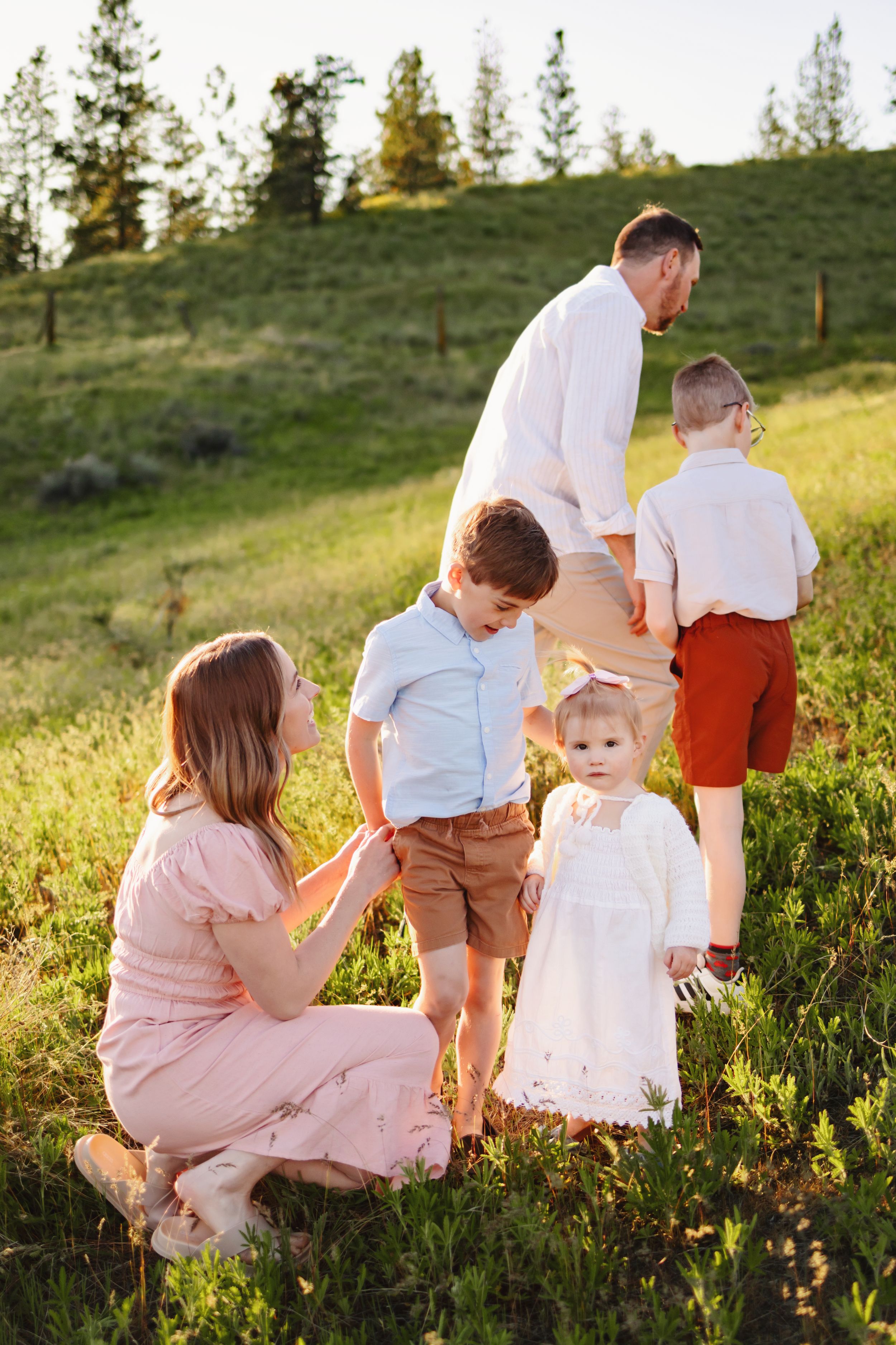 Family enjoying a sunset moment together on a grassy hillside with pine trees in the background during golden hour.