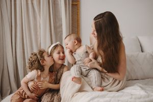 A joyful family moment with siblings and parent sharing laughter while relaxing together on a white bed.