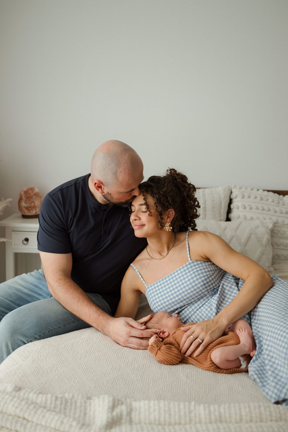 A couple sits on a bed, tenderly gazing at their newborn baby, sharing a warm and intimate family moment.