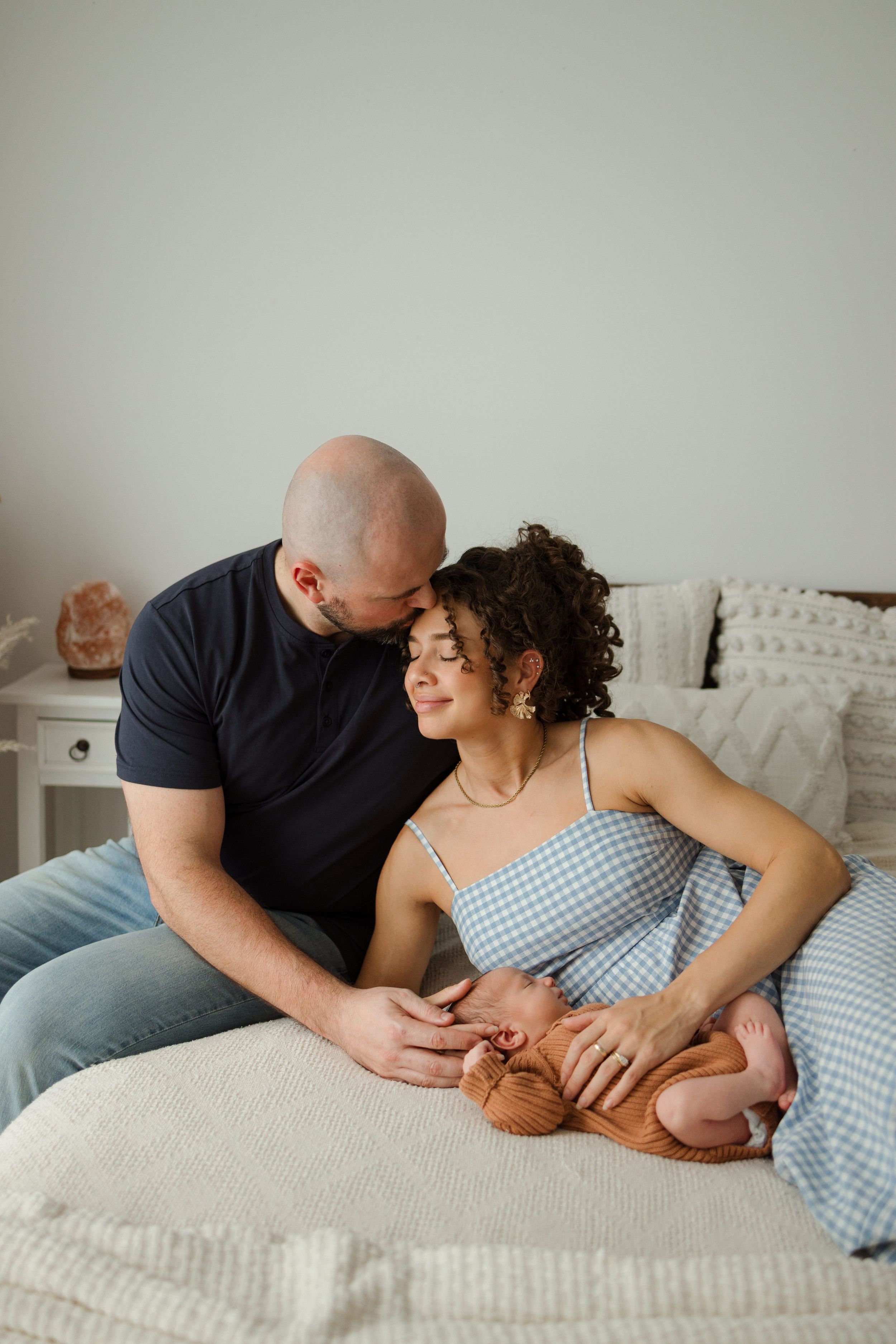 A couple sits on a bed, tenderly gazing at their newborn baby, sharing a warm and intimate family moment.