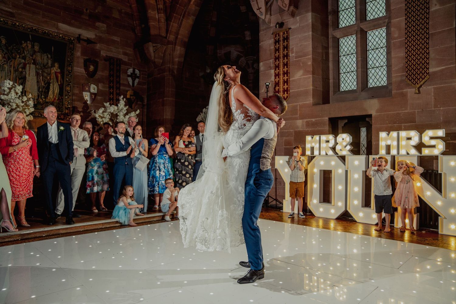 Couple shares their first dance at wedding reception with illuminated marquee letters in background.