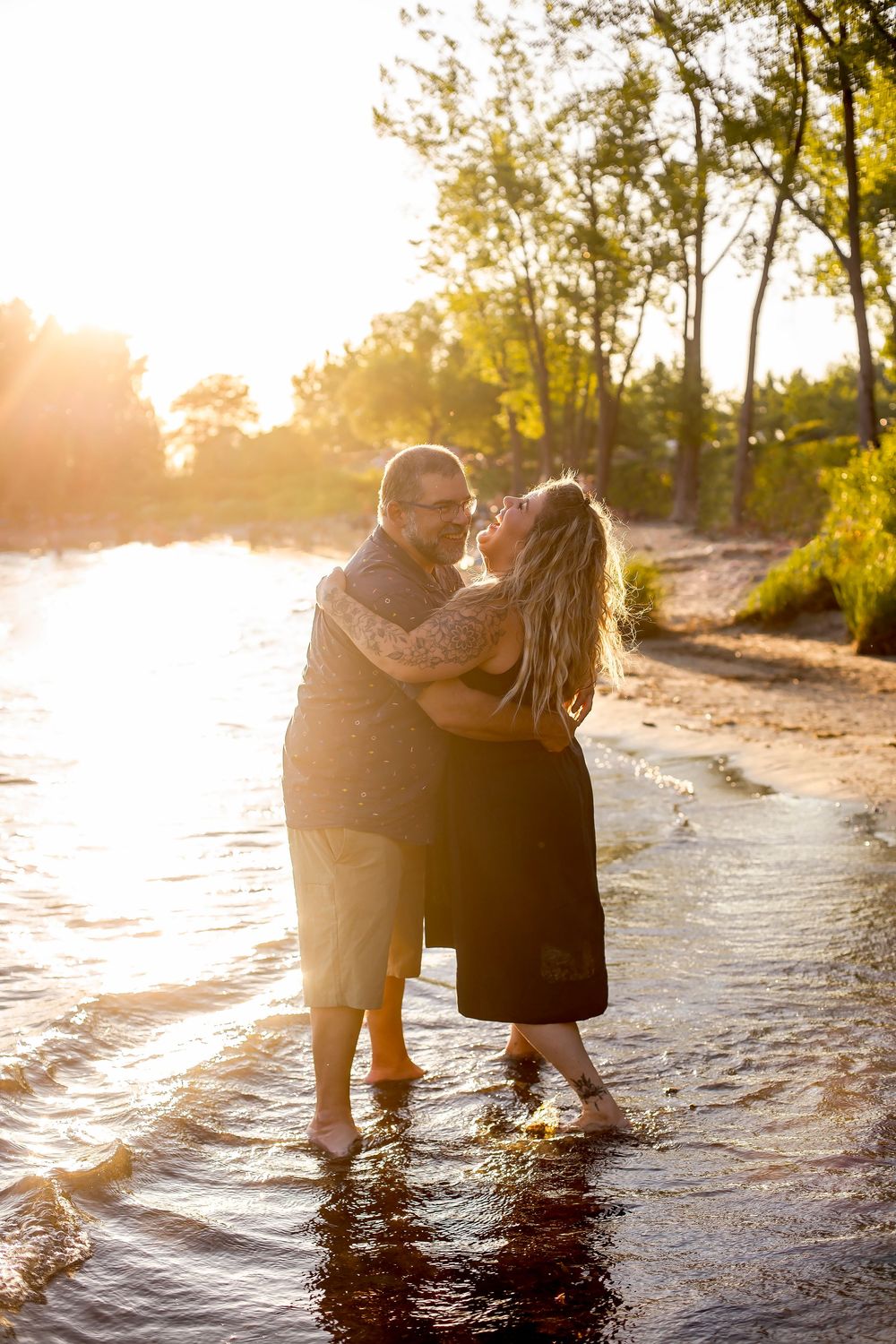 A couple embraces while standing in a shallow river, bathed in warm golden sunset light.