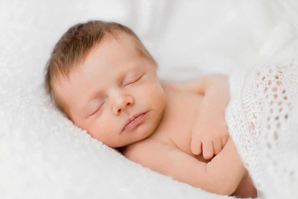 Peaceful newborn baby sleeping soundly on a soft white knit blanket in a serene and tender portrait.