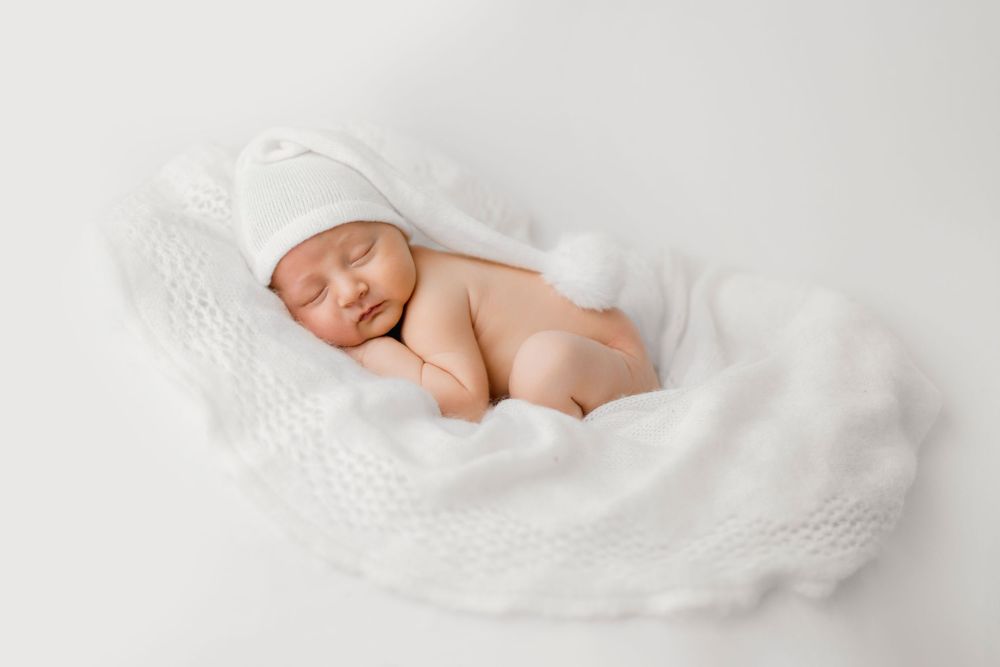 Nouveau-né paisible dormant dans un bol en tricot blanc, coiffé d'un bonnet blanc, sur un fond blanc.