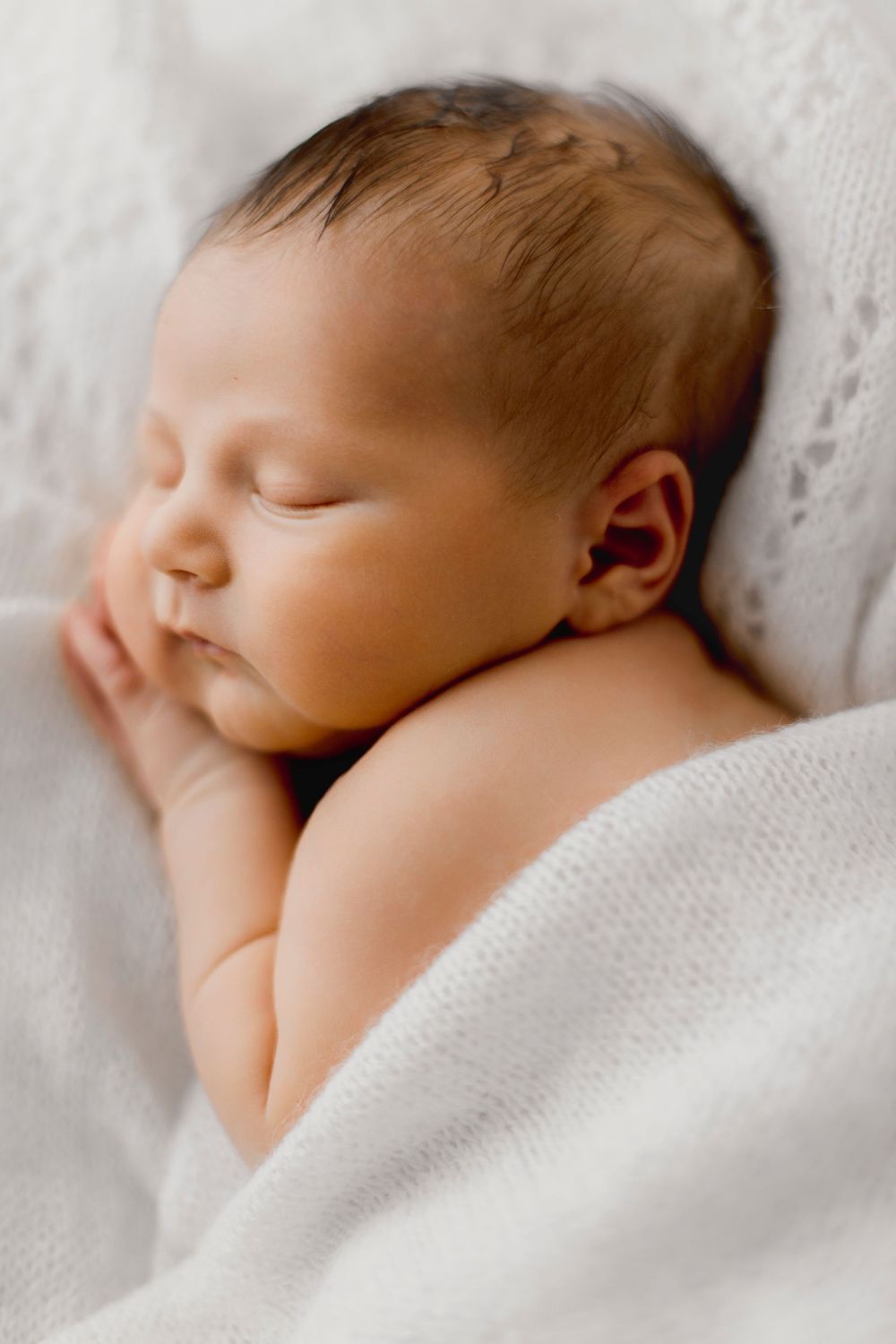 A peaceful newborn baby sleeping soundly wrapped in a soft white knit blanket.