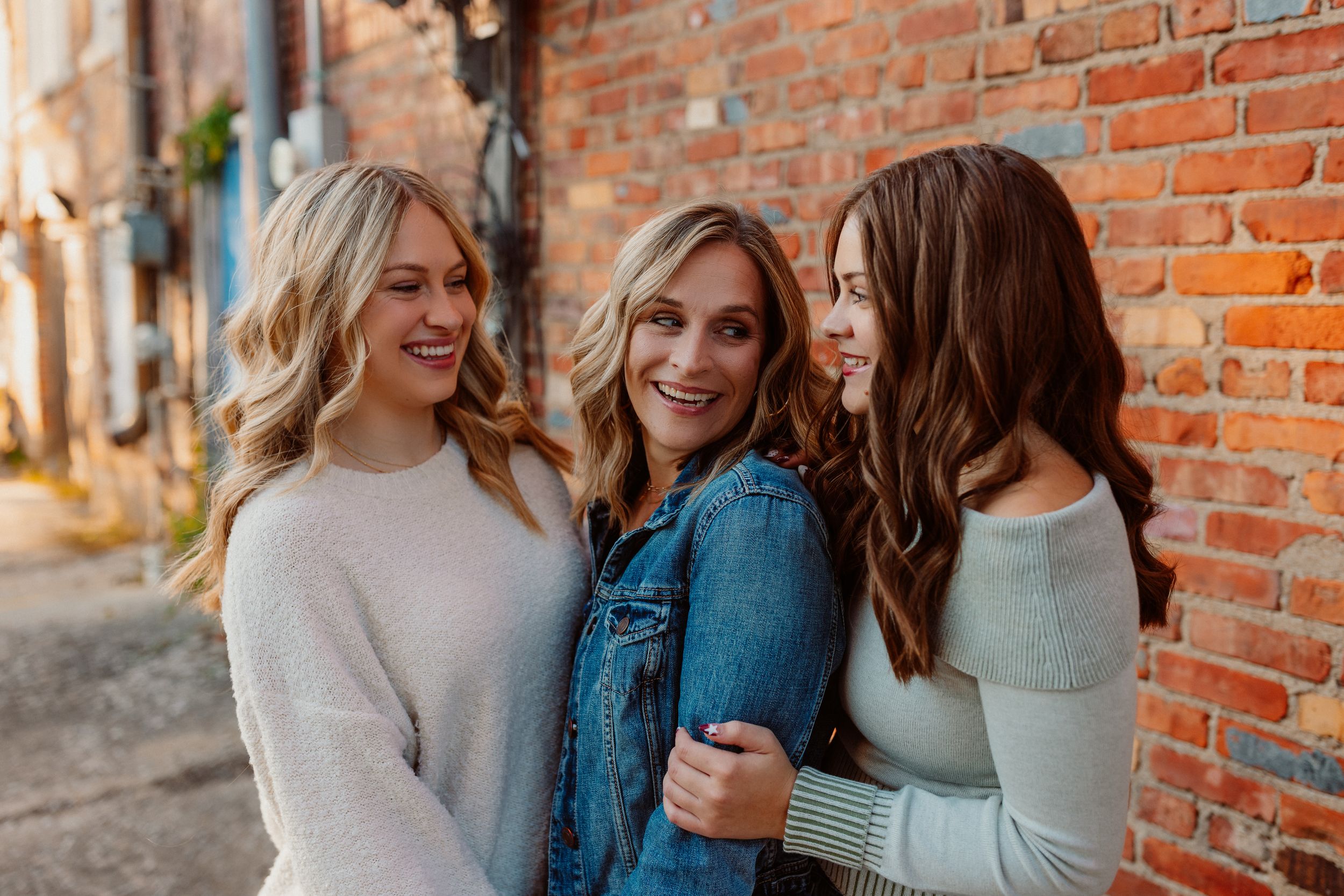 Kansas family in casual sweaters sharing joyful moments against brick wall.