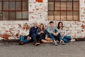 Group photo session with family sitting casually against weathered brick wall in Paola, Kansas