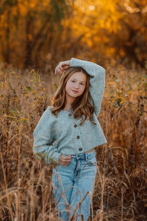 Children's portrait in gray sweater and jeans poses in autumn field with golden bokeh Kansas background.