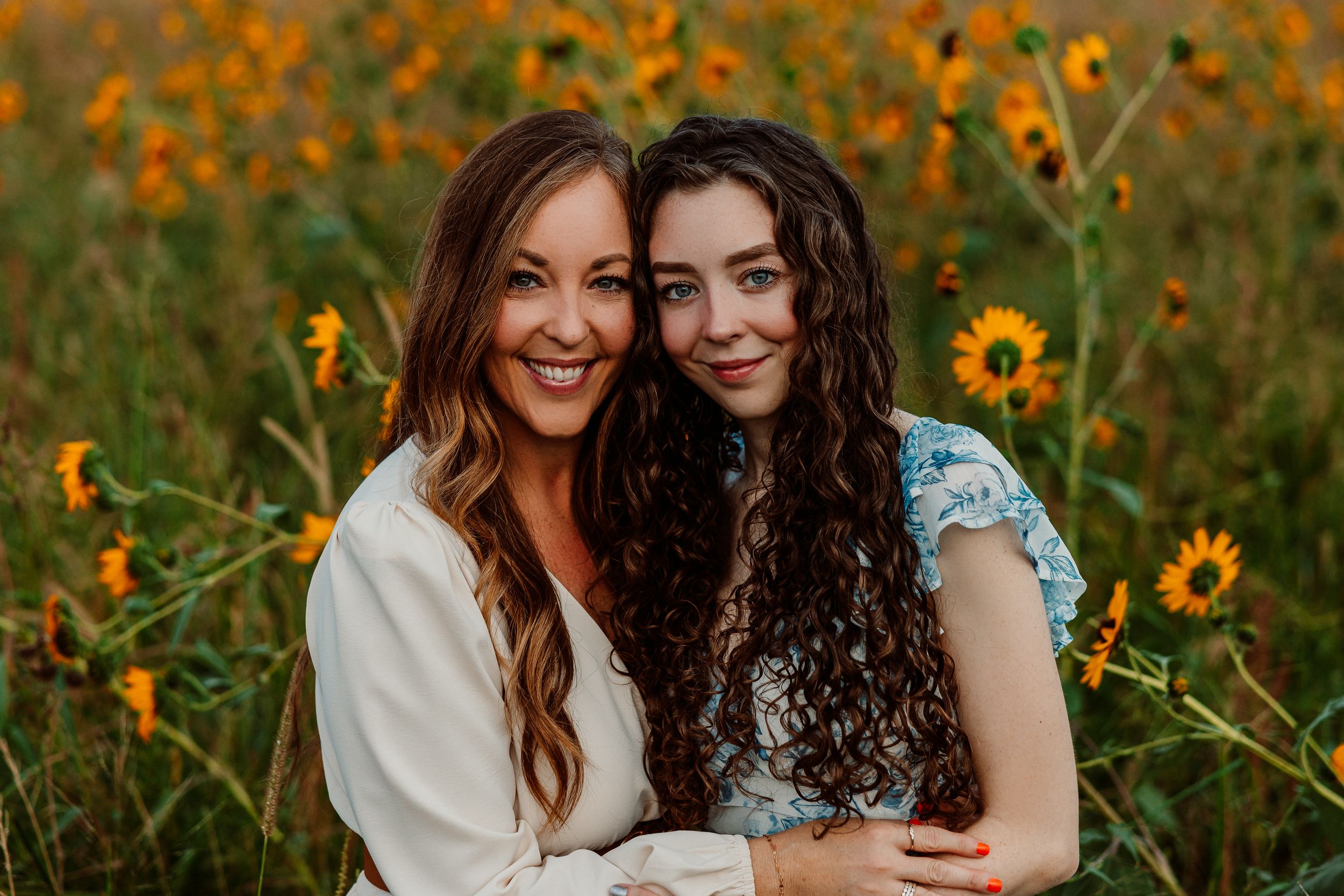 Two people pose together in a field of bright yellow wildflowers during Kansas golden hour.
