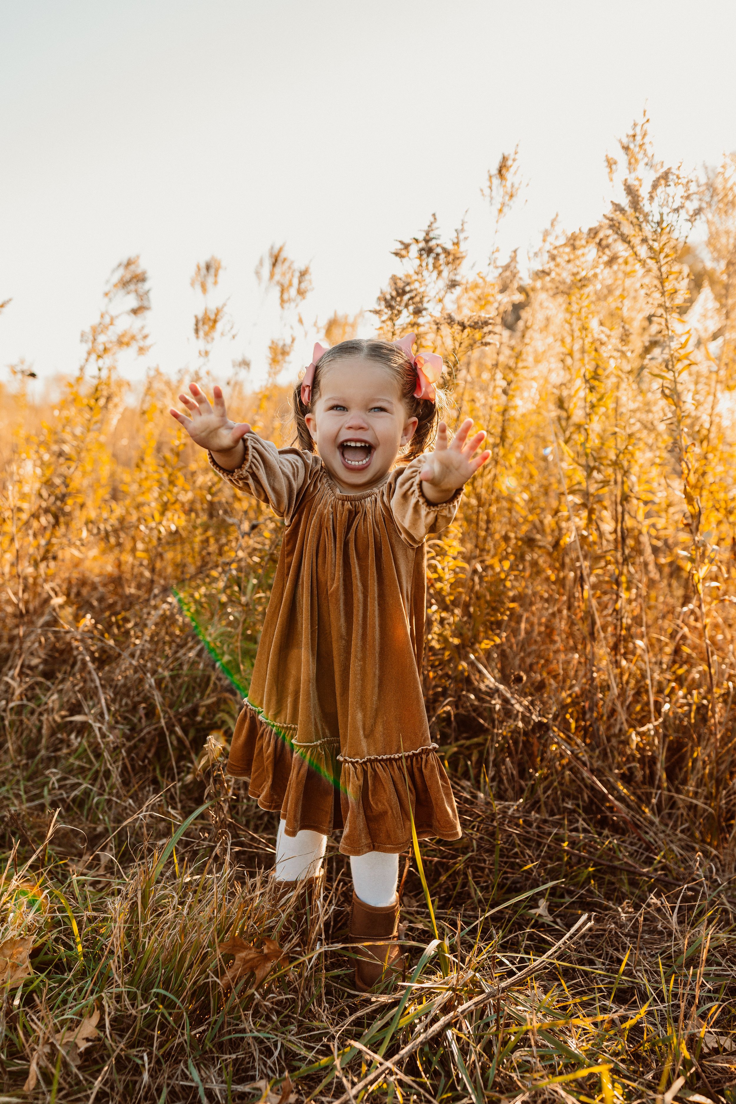 Child in brown dress playing joyfully in tall golden grass at sunset in Oalthe, Kansas.