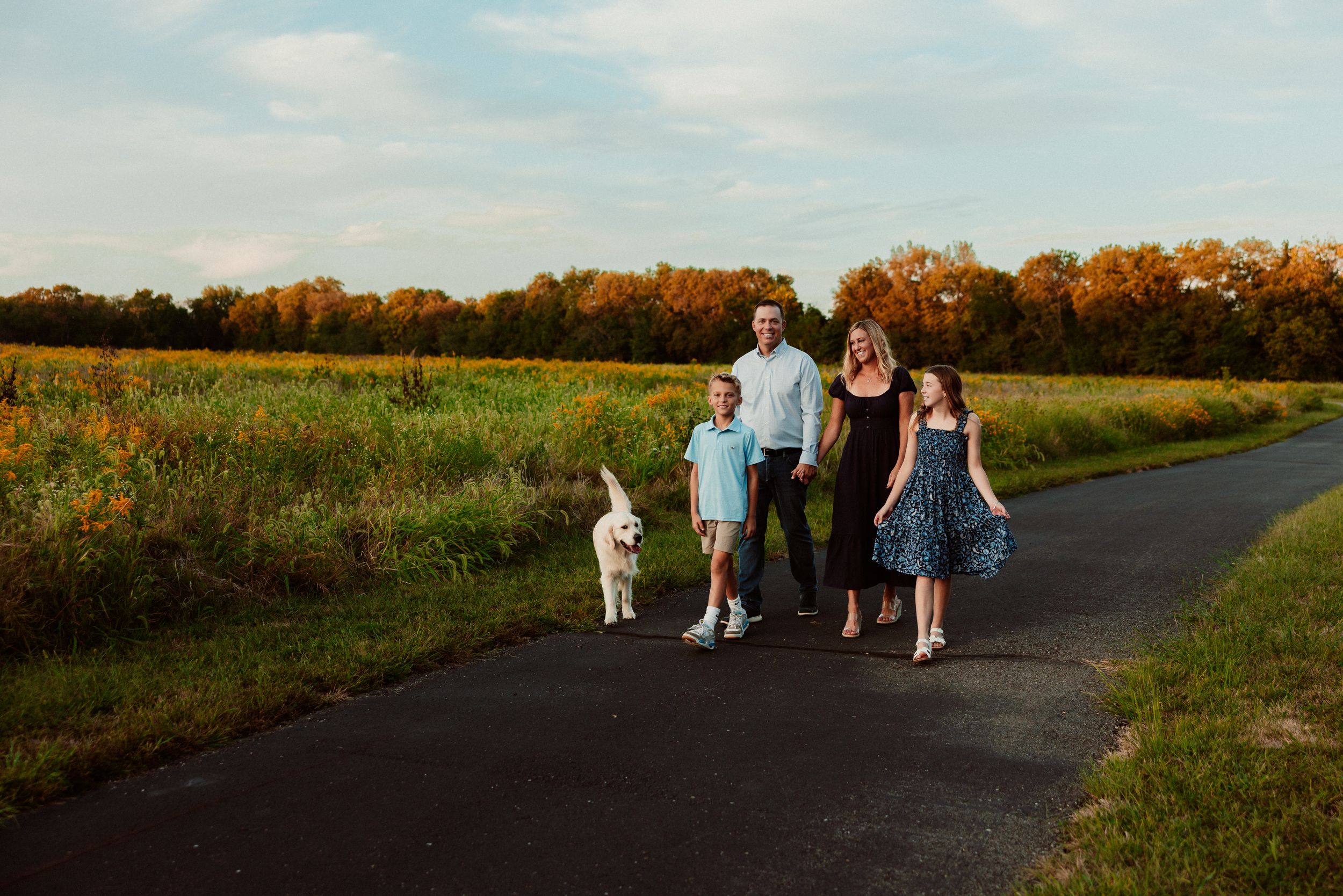 Family walking together on a paved path surrounded by autumn fields at sunset in Stilwell, Kansas,