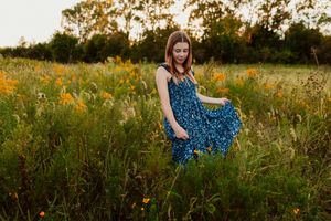 Girl in blue dress walking through wildflower meadow during Kansas golden hour.