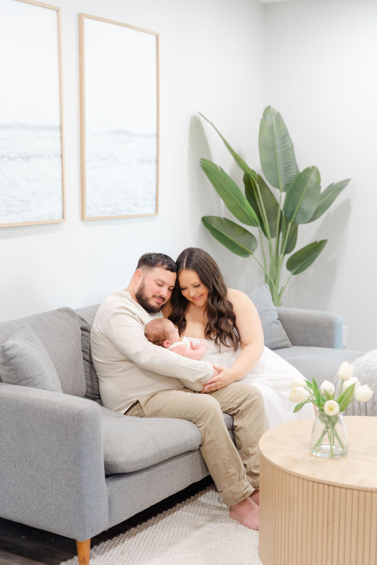 newborn baby cuddle up in mom and dads arms sitting on the couch during their newborn session in Tampa florida