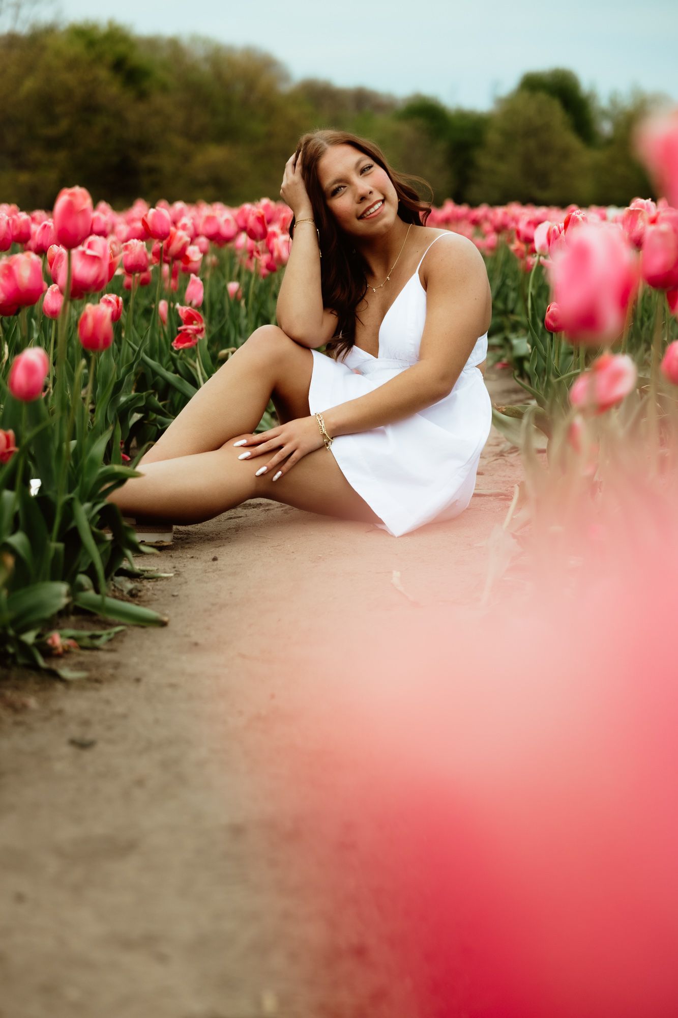 Portrait of someone in a white dress sitting among pink wildflowers in a summer meadow.