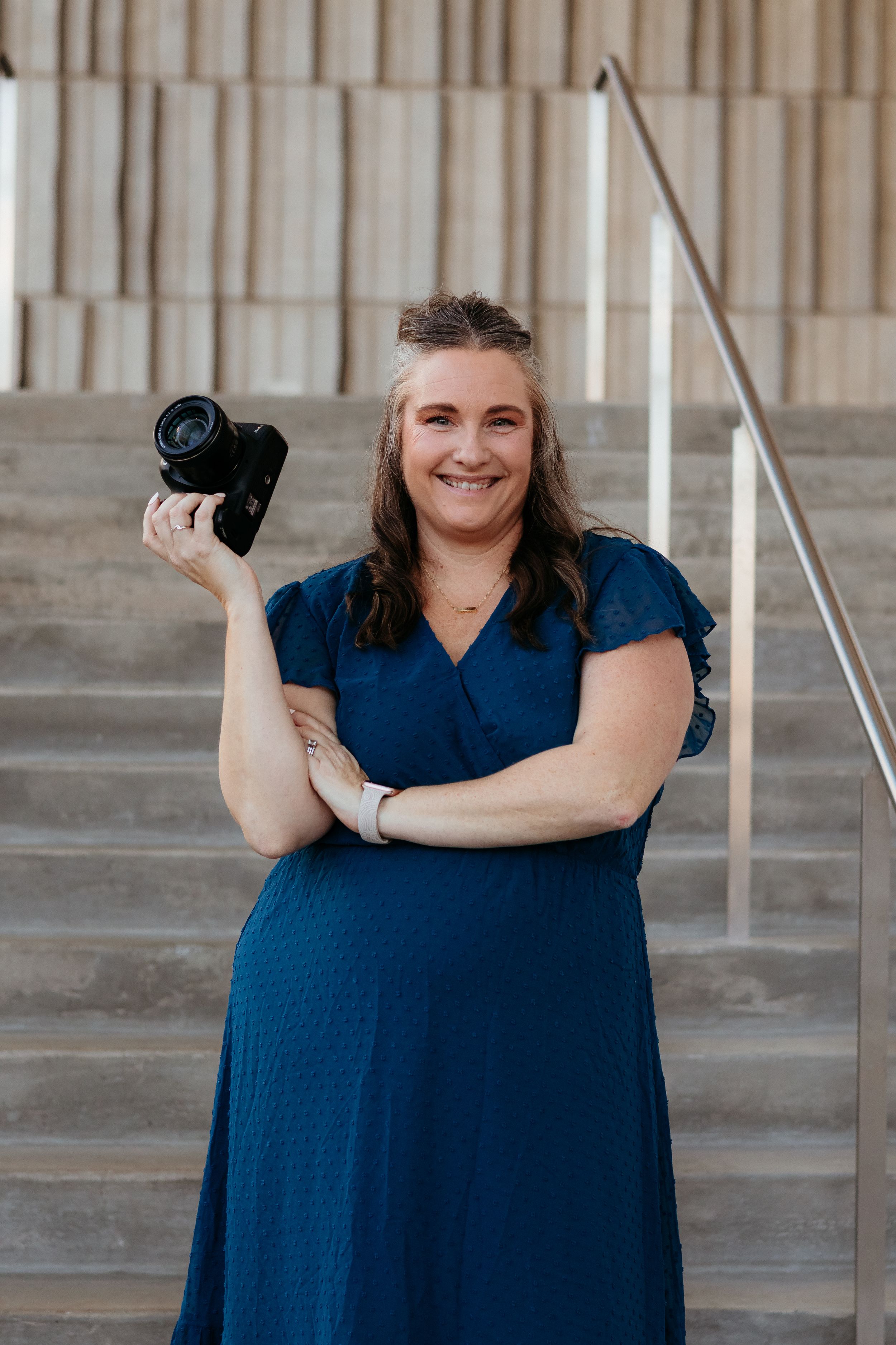 Marion photographer Nichole Sieck Photography stands with a camera in her hand smiling on concrete stairs.