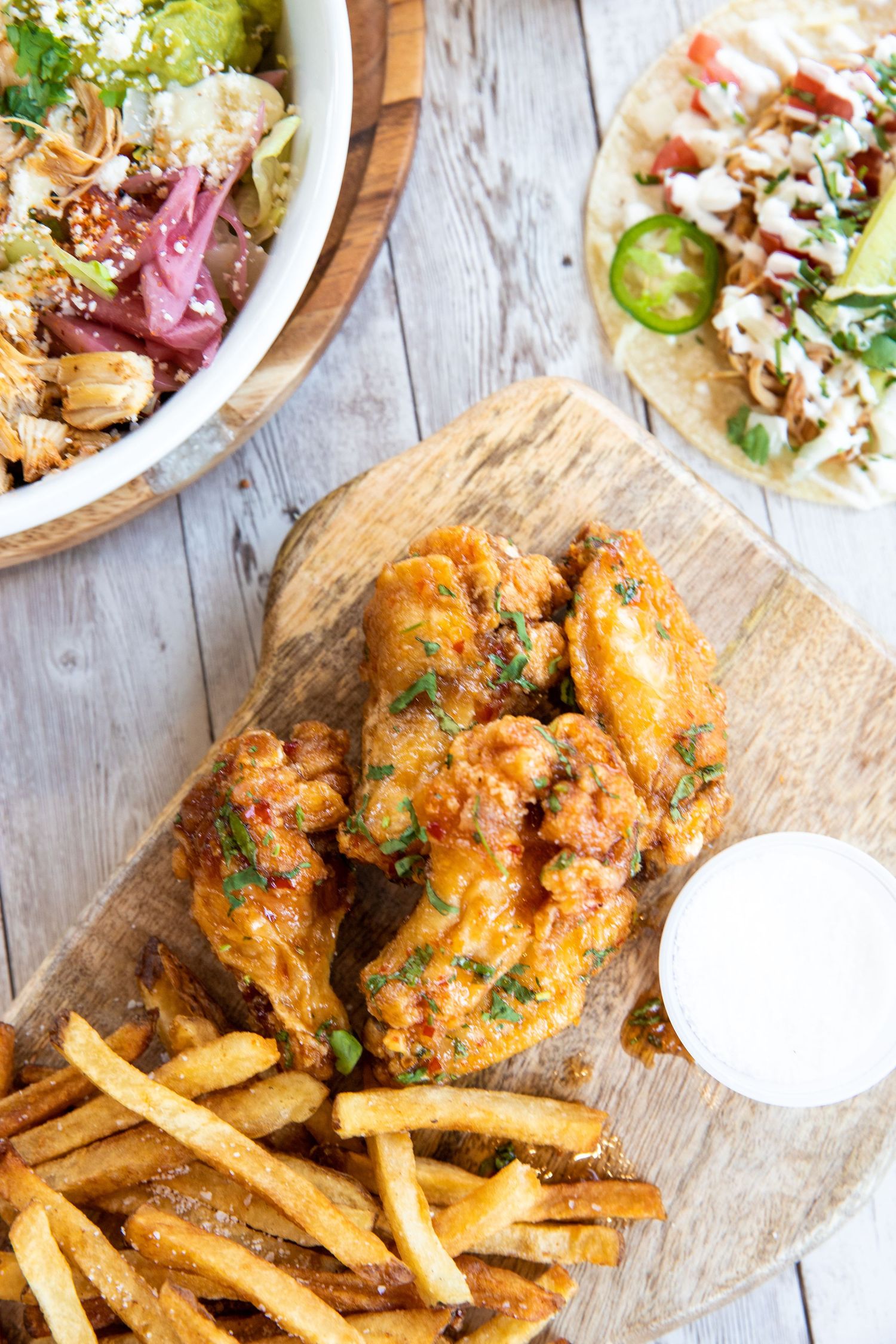 Golden fried chicken strips served with french fries and colorful sides on rustic wooden board.