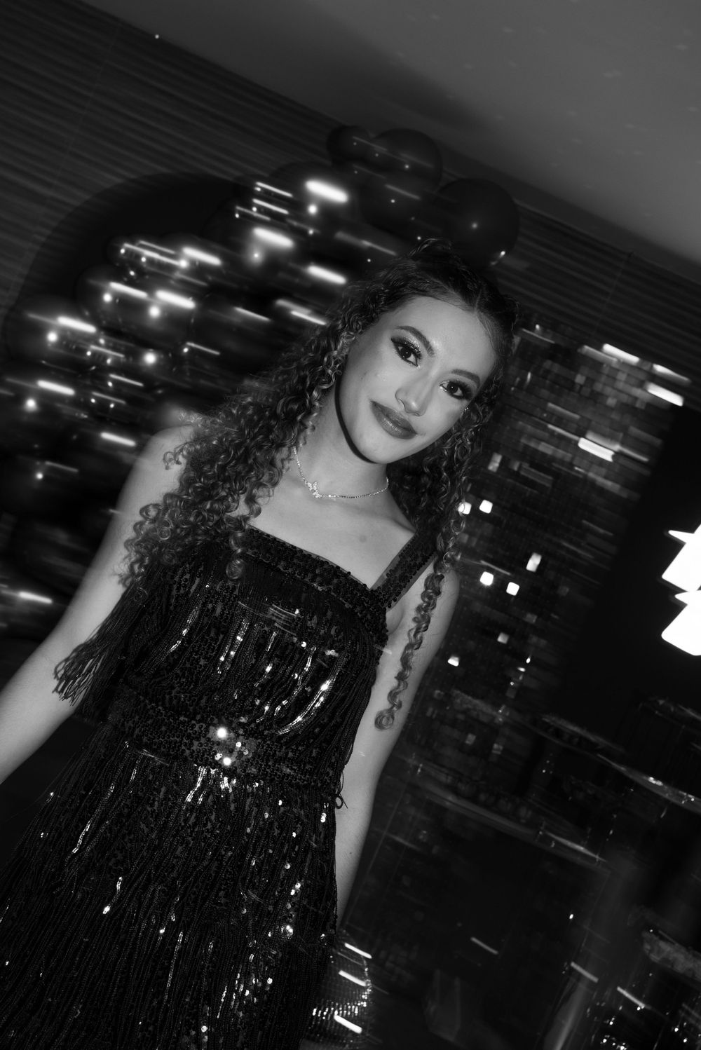 Woman in a sparkling black dress poses against a backdrop of twinkling lights.