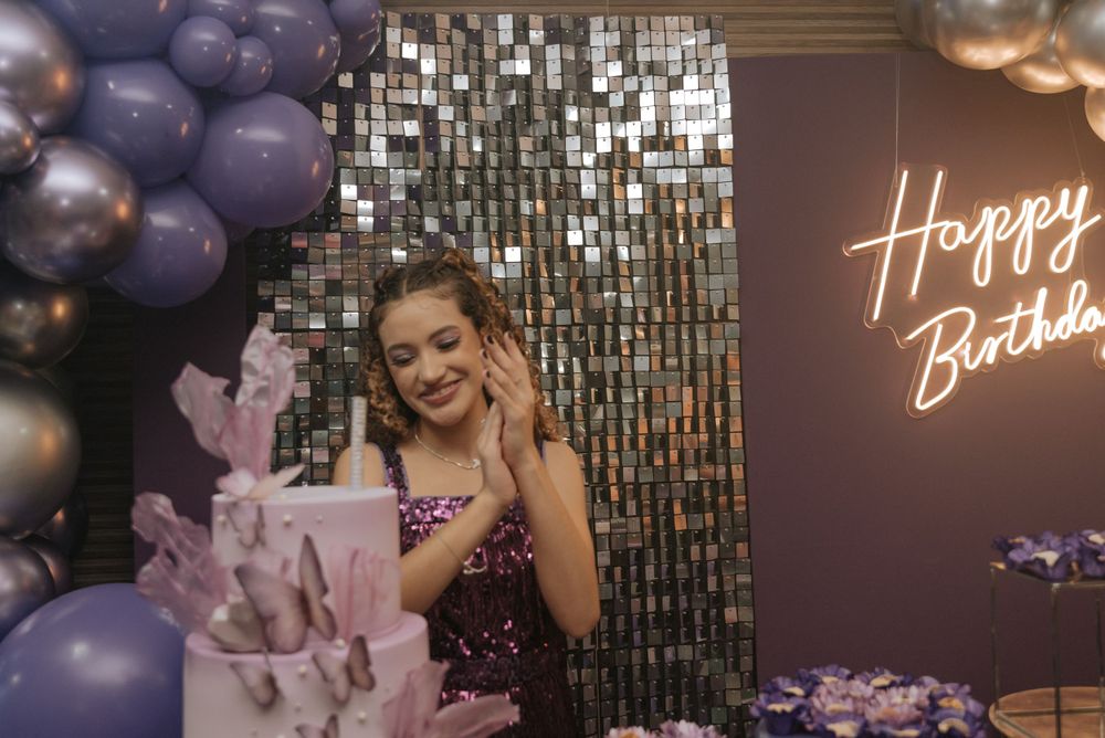 Celebration scene with purple balloons, metallic backdrop, and a happy birthday neon sign.