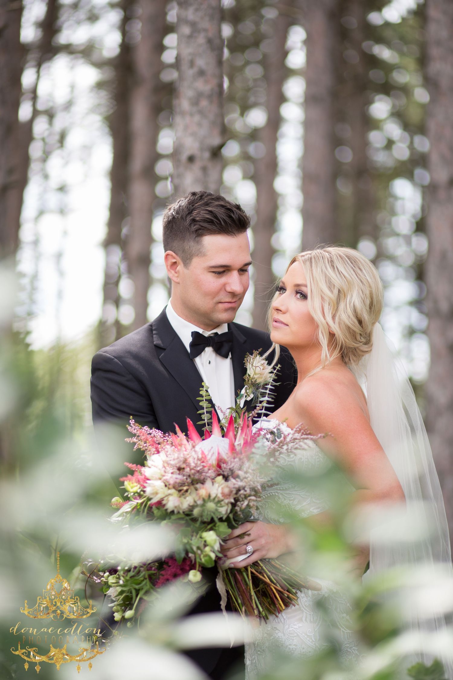 Bride and groom sharing an intimate moment in a forest holding a lush pink and green bouquet.