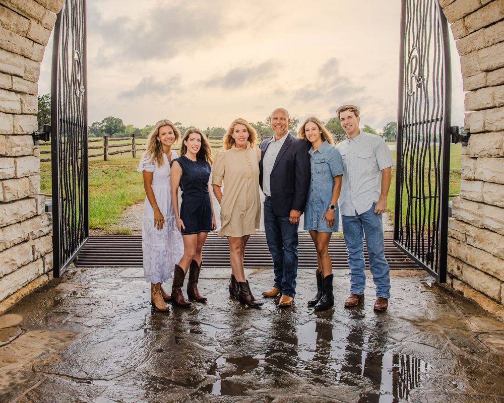 Group of people standing in an open stone gateway on wet ground with fence and countryside views behind them.