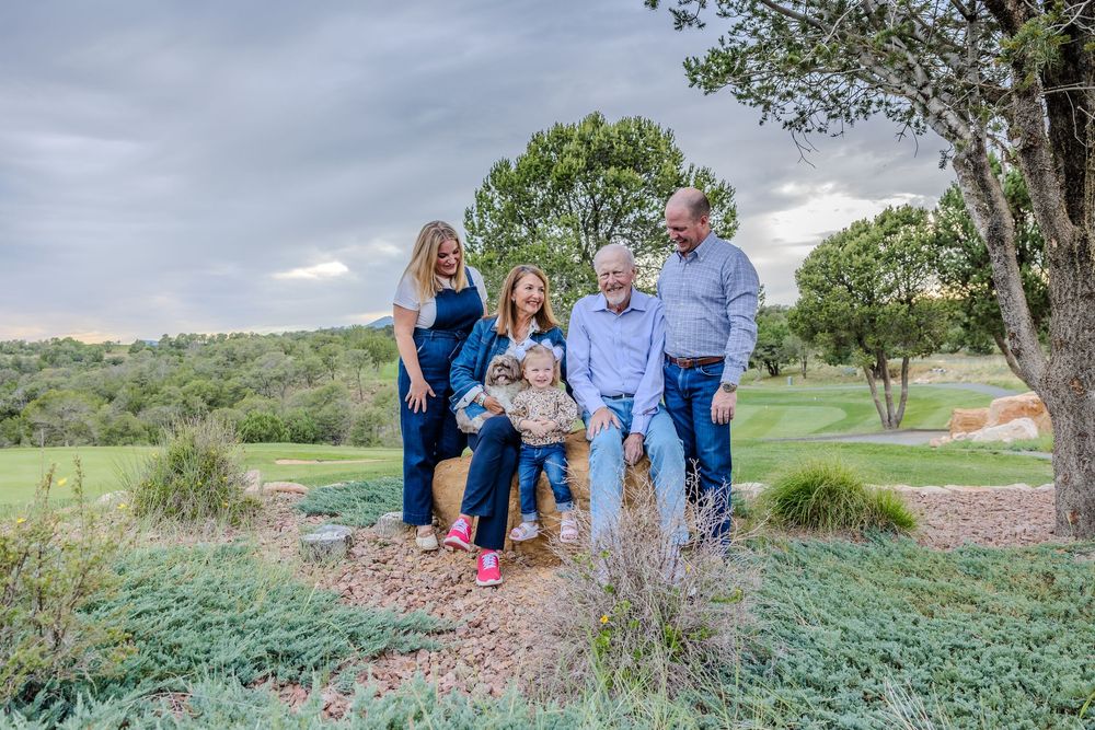 Family poses together outdoors in a natural landscape with green rolling hills and trees in the background.