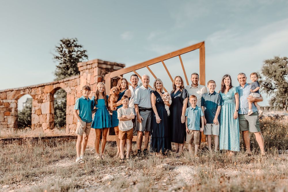 Wedding party poses outdoors by stone ruins with wooden arch frame in warm sunset light.