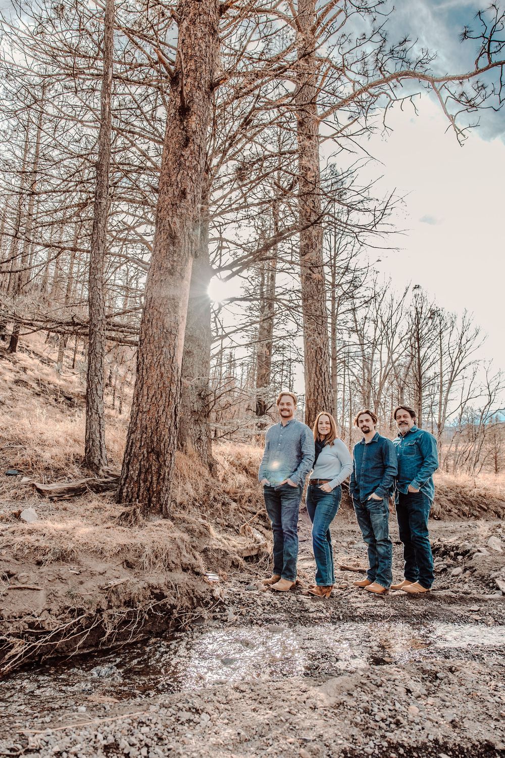 Group of people standing in a forest on a dirt path with tall trees and natural sunlight filtering through branches.