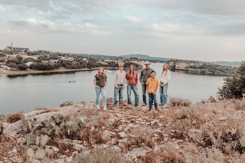 Group of friends standing on rocky overlook at sunset with lake view and rolling hills in background.