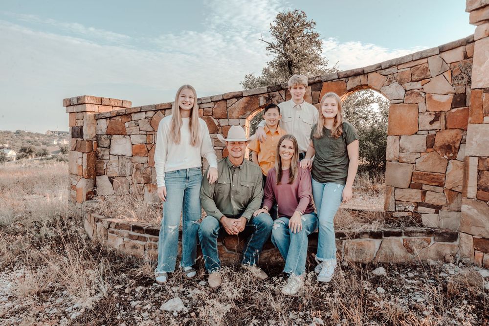 A group poses together on stone ruins in a rustic outdoor setting at sunset with vintage aesthetic tones.
