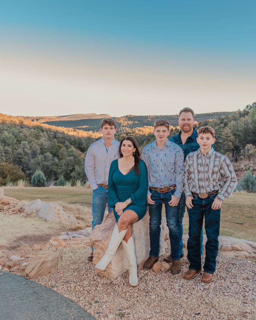 Group stands together on rocky terrain at sunset with rolling hills and trees in the background.