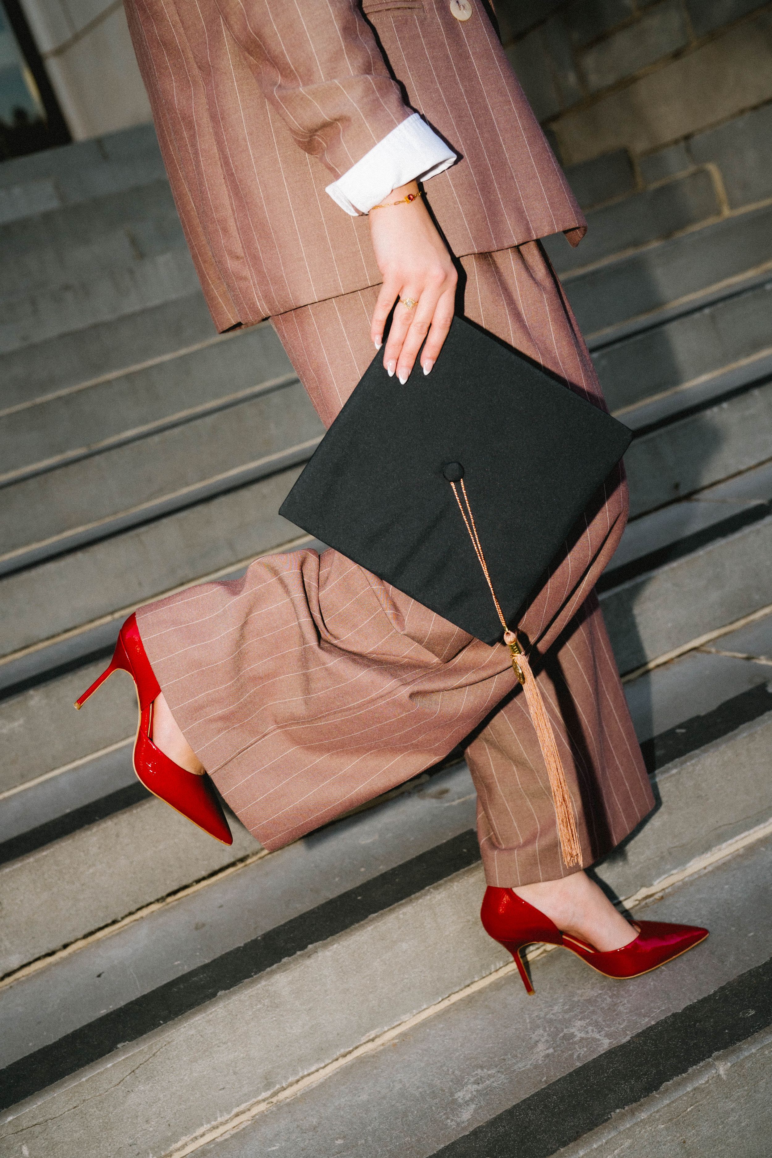 Woman in striped suit and red heels walking up steps holding a black graduation cap.