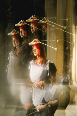 Multiple exposure photo of a red-haired woman in a gray dress holding drumsticks in an artistic blur effect.