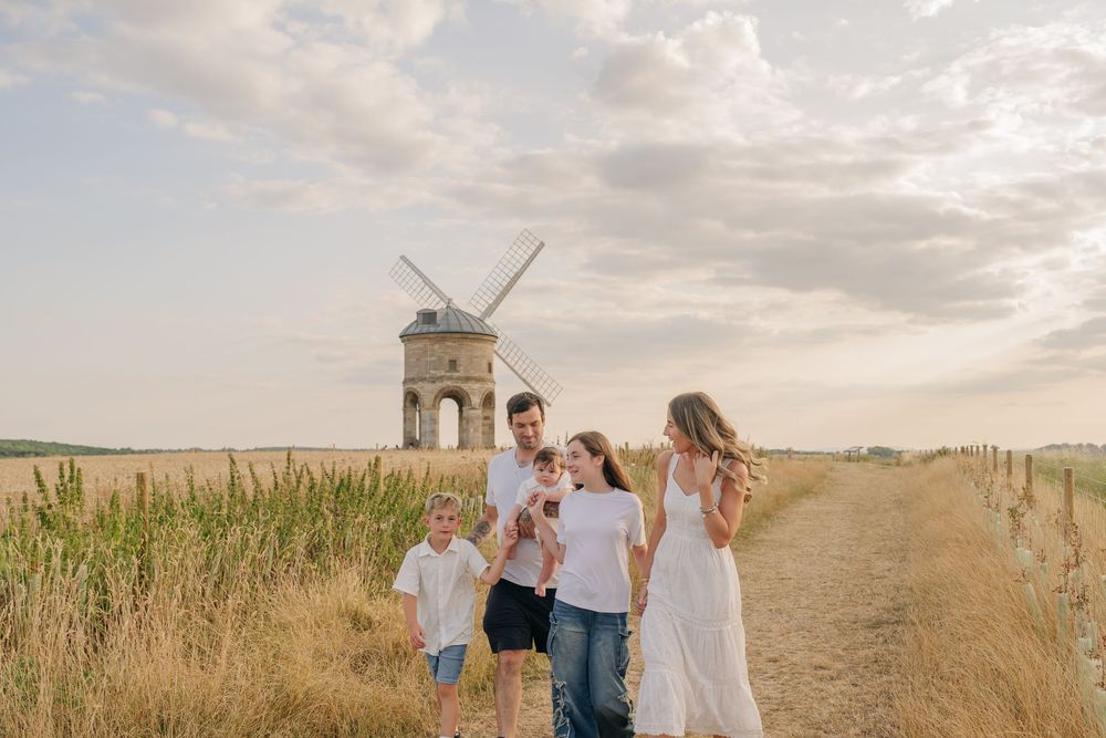 Family of four walking near a historic windmill on a sunny day in a golden field.