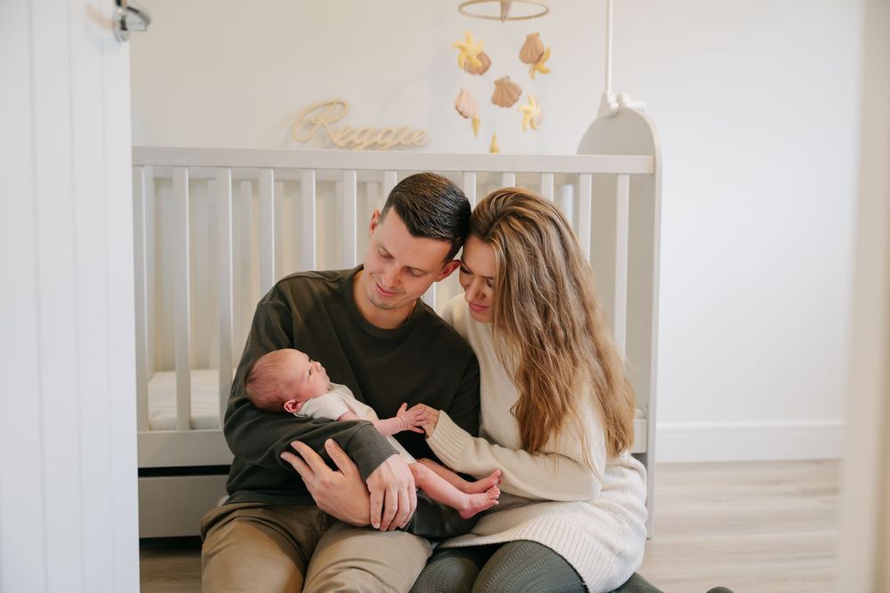 A tender family moment in a nursery as parents share a kiss while holding their newborn baby.