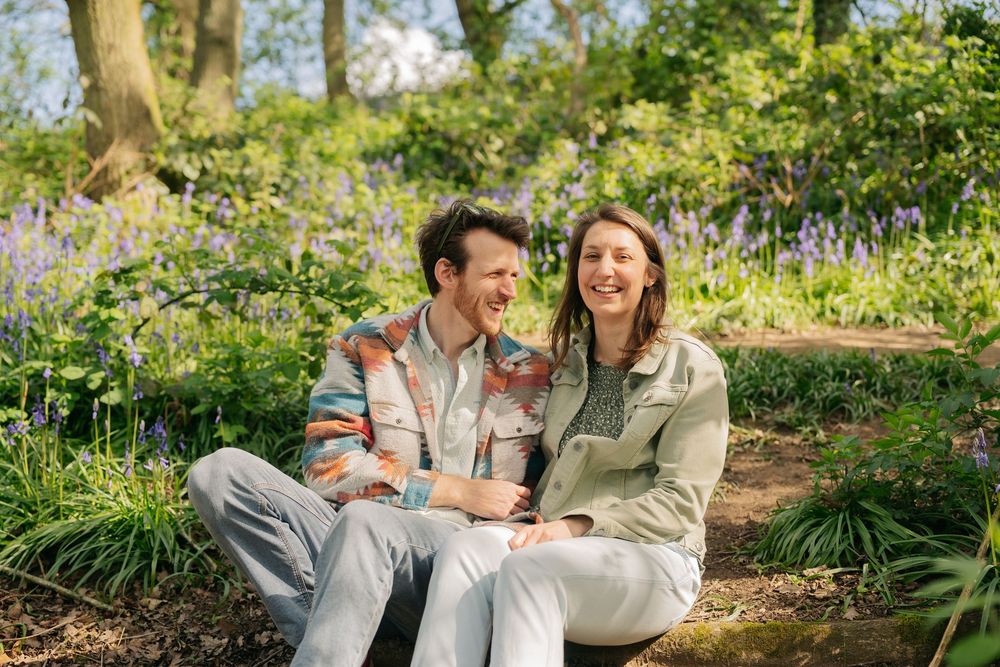 Happy couple laughing together outdoors in a bluebell woodland garden on a sunny spring day.