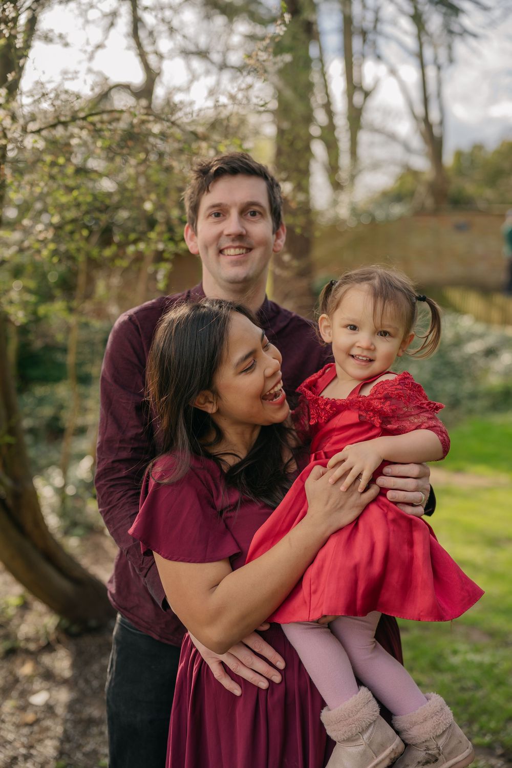 A family shares joyful moments together outdoors in coordinating burgundy and red outfits during a photo session.