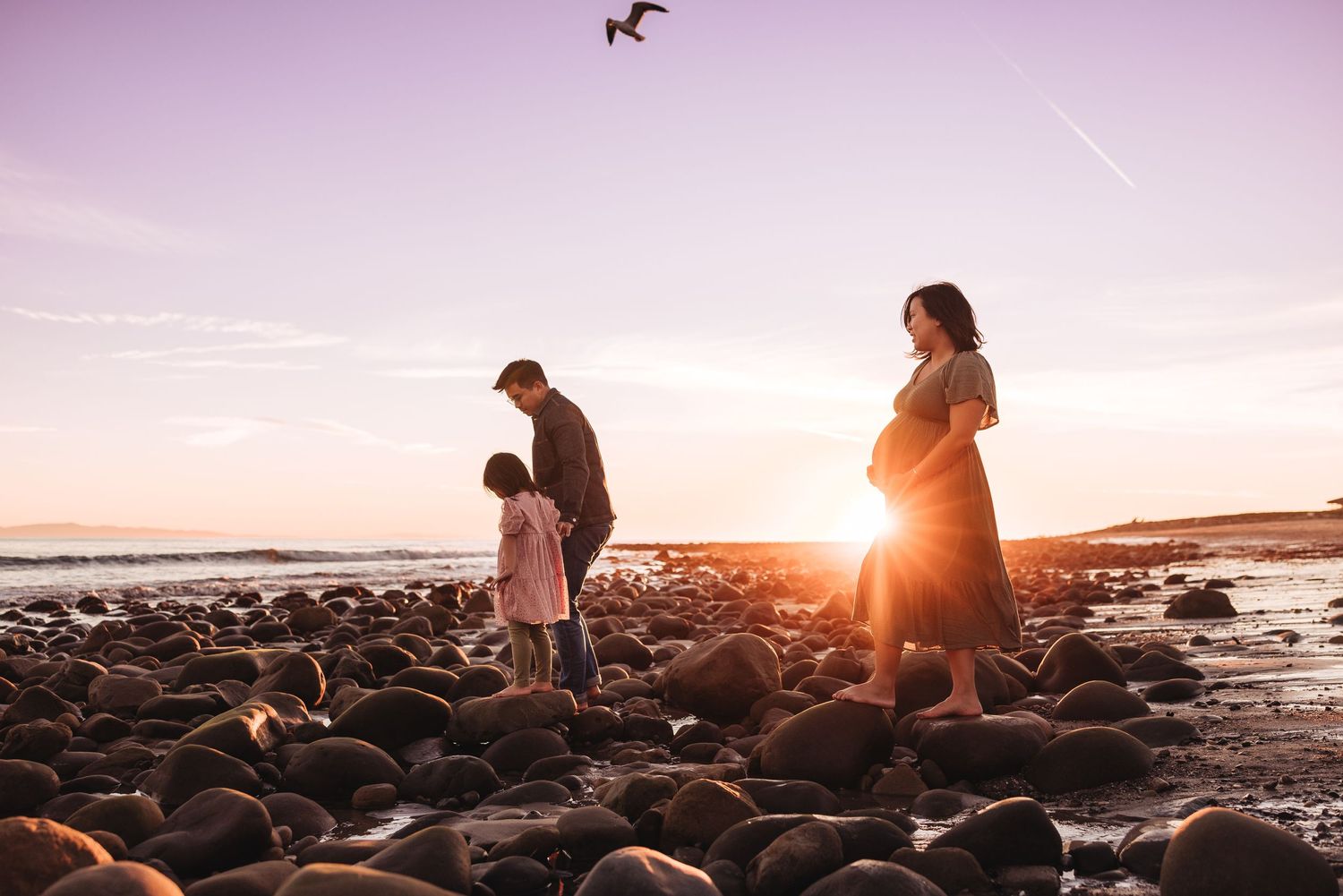 Silhouettes of a couple against dramatic coastal sunset with birds flying overhead.