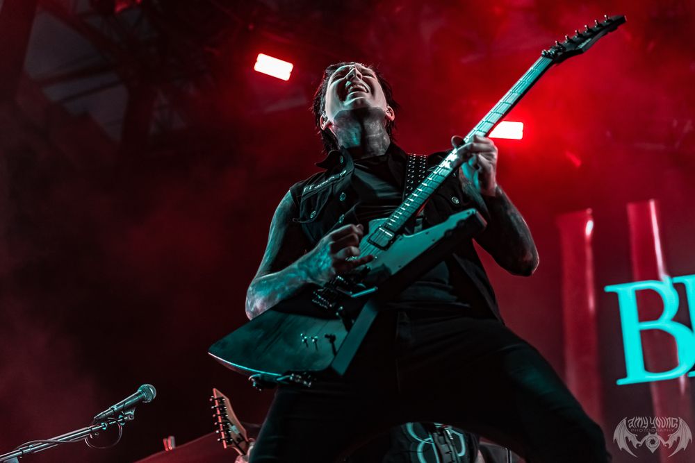 Musician playing guitar on stage illuminated by intense red spotlights and atmospheric haze.