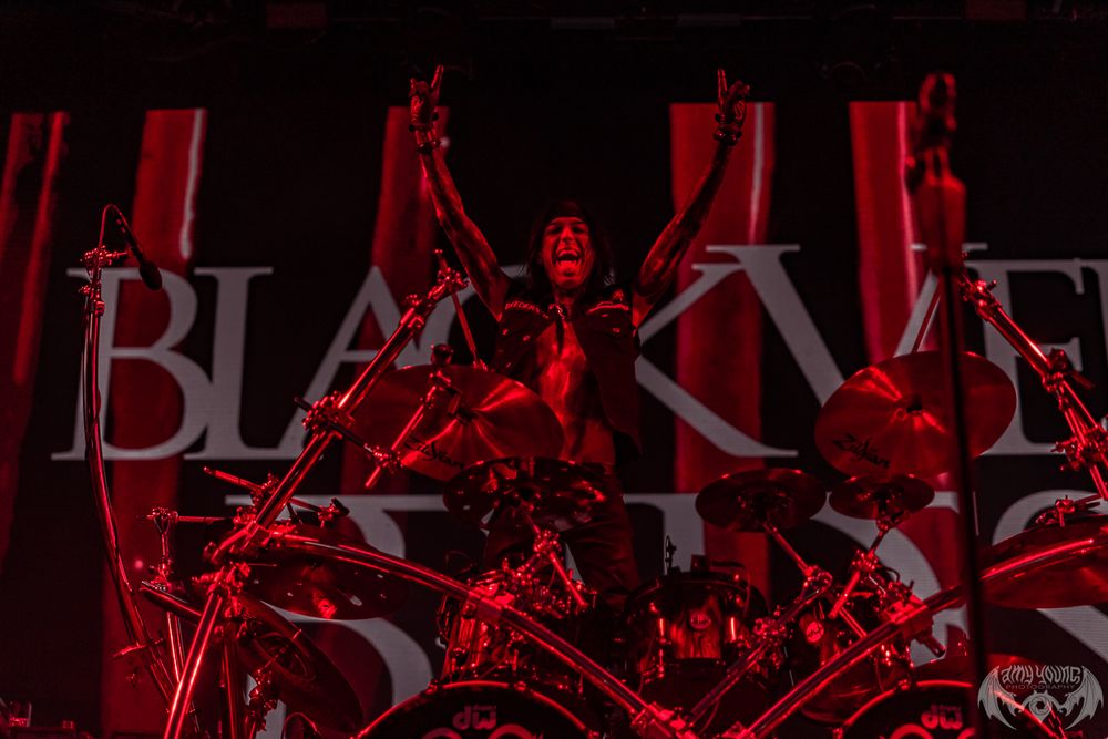 Dark concert stage setup with red lighting and band equipment silhouettes visible.