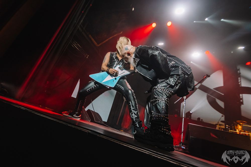 An energetic performer bends down on stage during a concert with dramatic red lighting and fog effects.