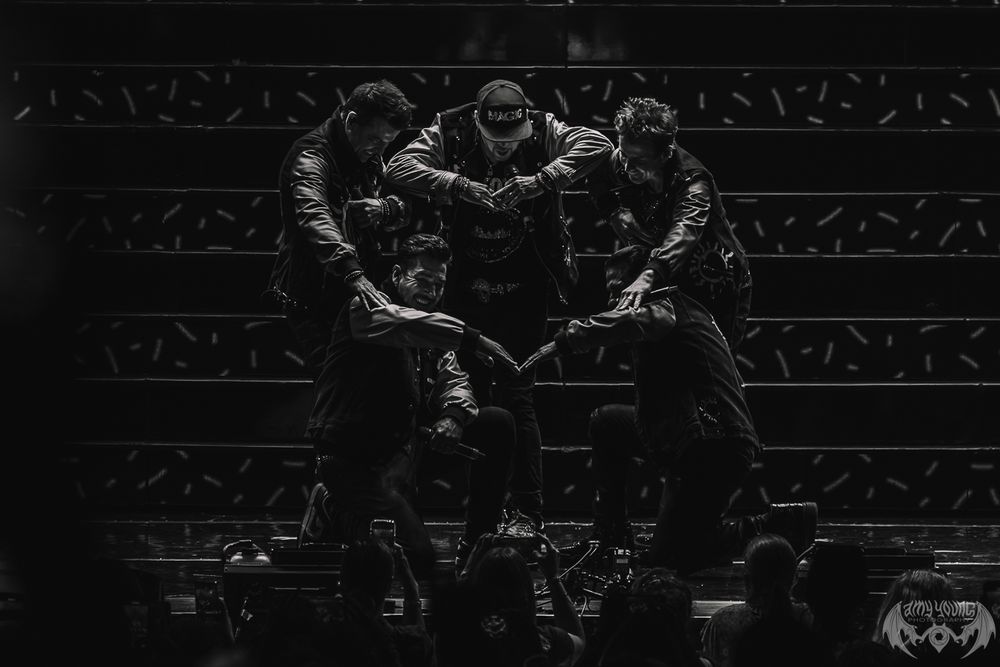 Dark concert venue with minimal lighting showing silhouettes of performers on stage.