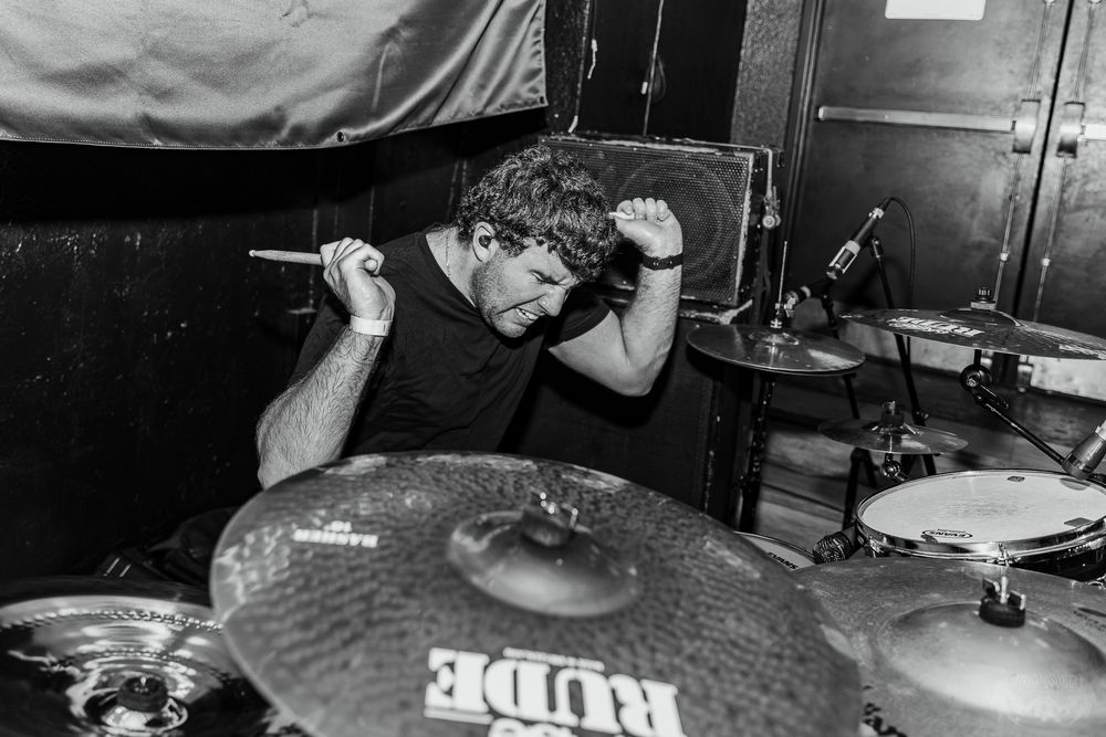 Drummer performing intensely behind drum kit in black and white photography.