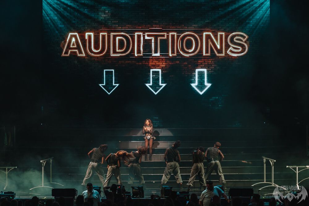 Stage setup with 'AUDITIONS' text display and dramatic teal lighting effects.