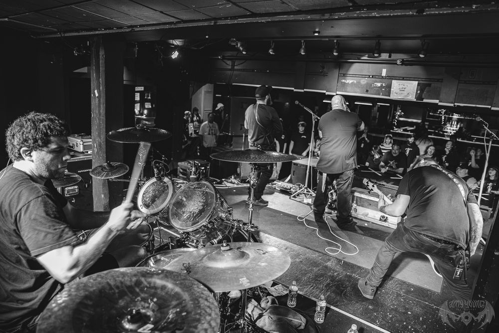 Band performing live on stage with multiple drummers in dark concert venue.