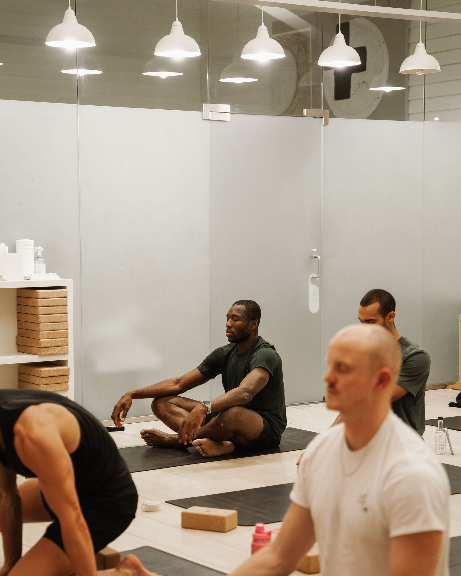 People practicing yoga or meditation in a modern studio space with pendant lighting and white walls.