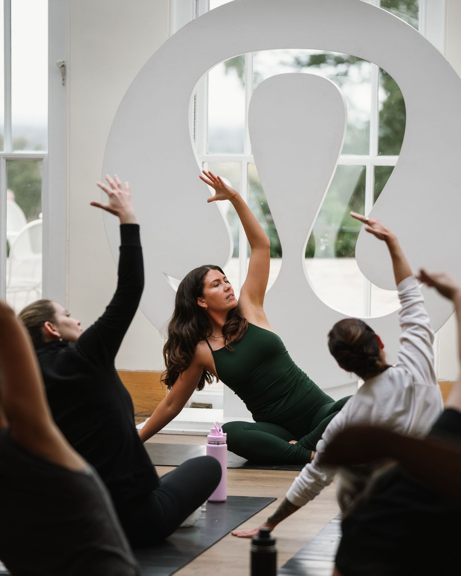 People practicing yoga and stretching together on mats in a bright studio room with a large decorative wall element.