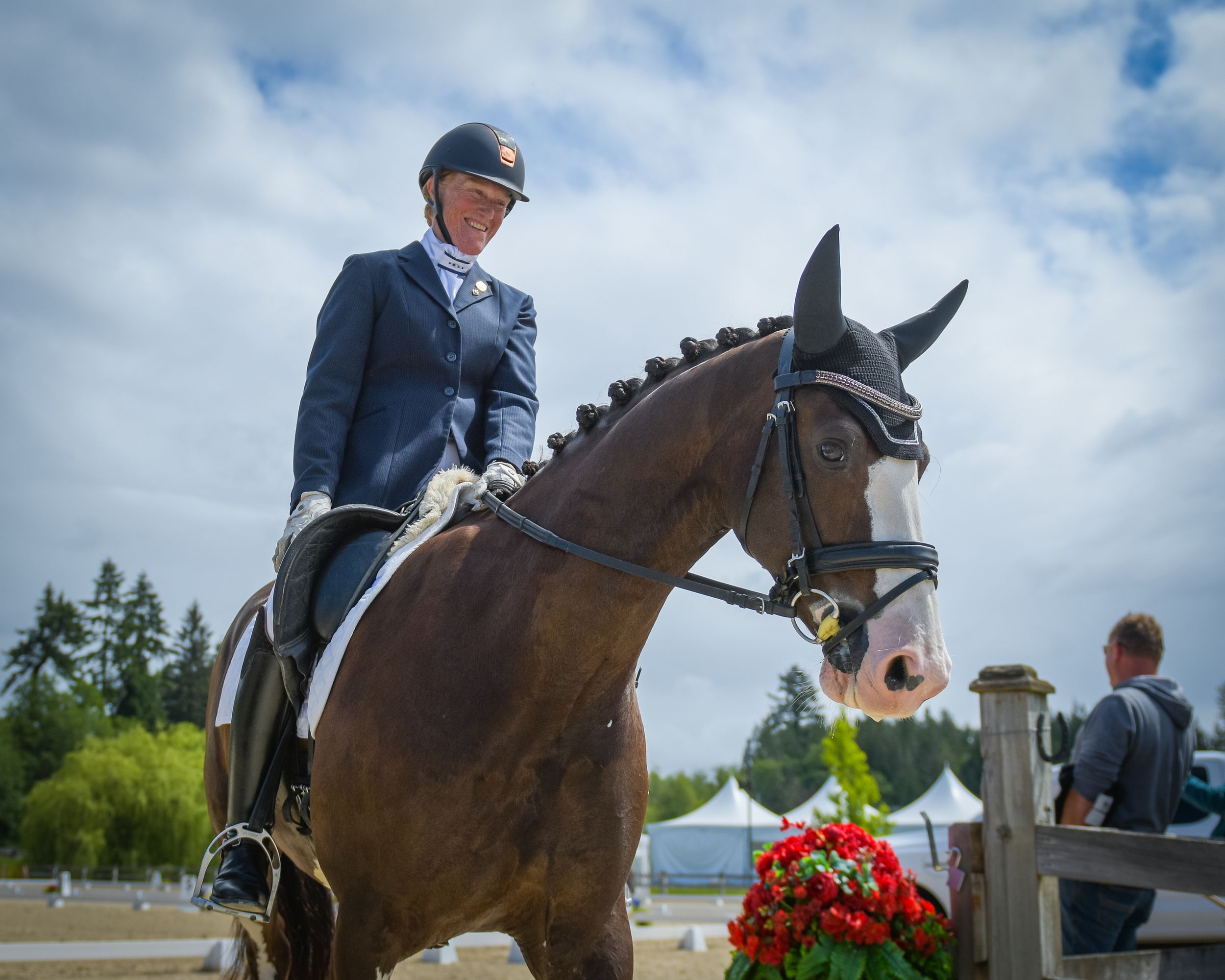 Equestrian rider in formal attire competing on a bay horse at an outdoor dressage competition with flowers.