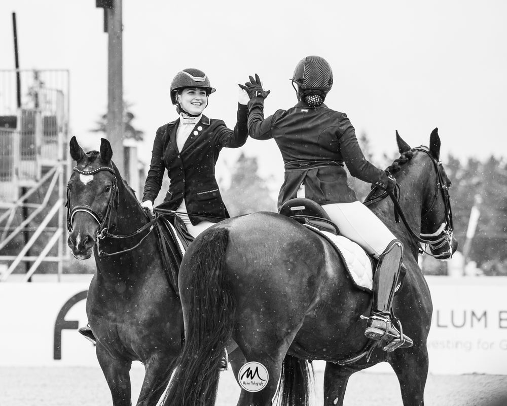 Two equestrians sharing a celebratory high-five while mounted on their horses during competition.