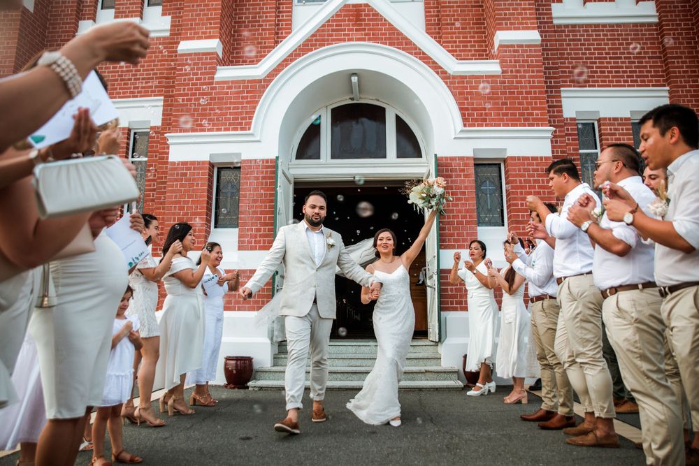 Wedding party in white and khaki creates celebration tunnel outside red brick church.